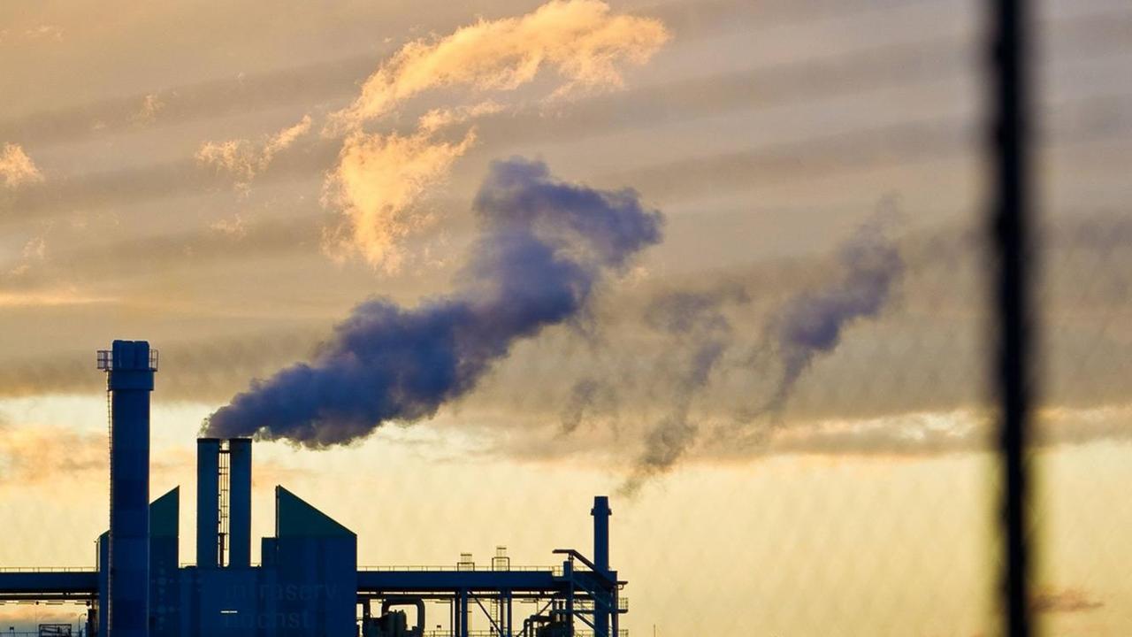 Rauchende Schornsteine im Industriepark Frankfurt-Höchst, darüber pastellfarbene Wolken, Abendsonne, im Vordergrund ein unscharfer Zaun. Rauchende Schornsteine im Industriepark Frankfurt-Höchst, darüber pastellfarbene Wolken, Abendsonne, im Vordergrund ein unscharfer Zaun.
