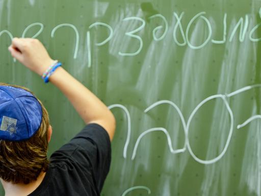 Ein Schüler der Talmud Tora Schule in Hamburg schreibt das Alphabet auf hebräisch an die Tafel. Unten steht das Wort "lernen".