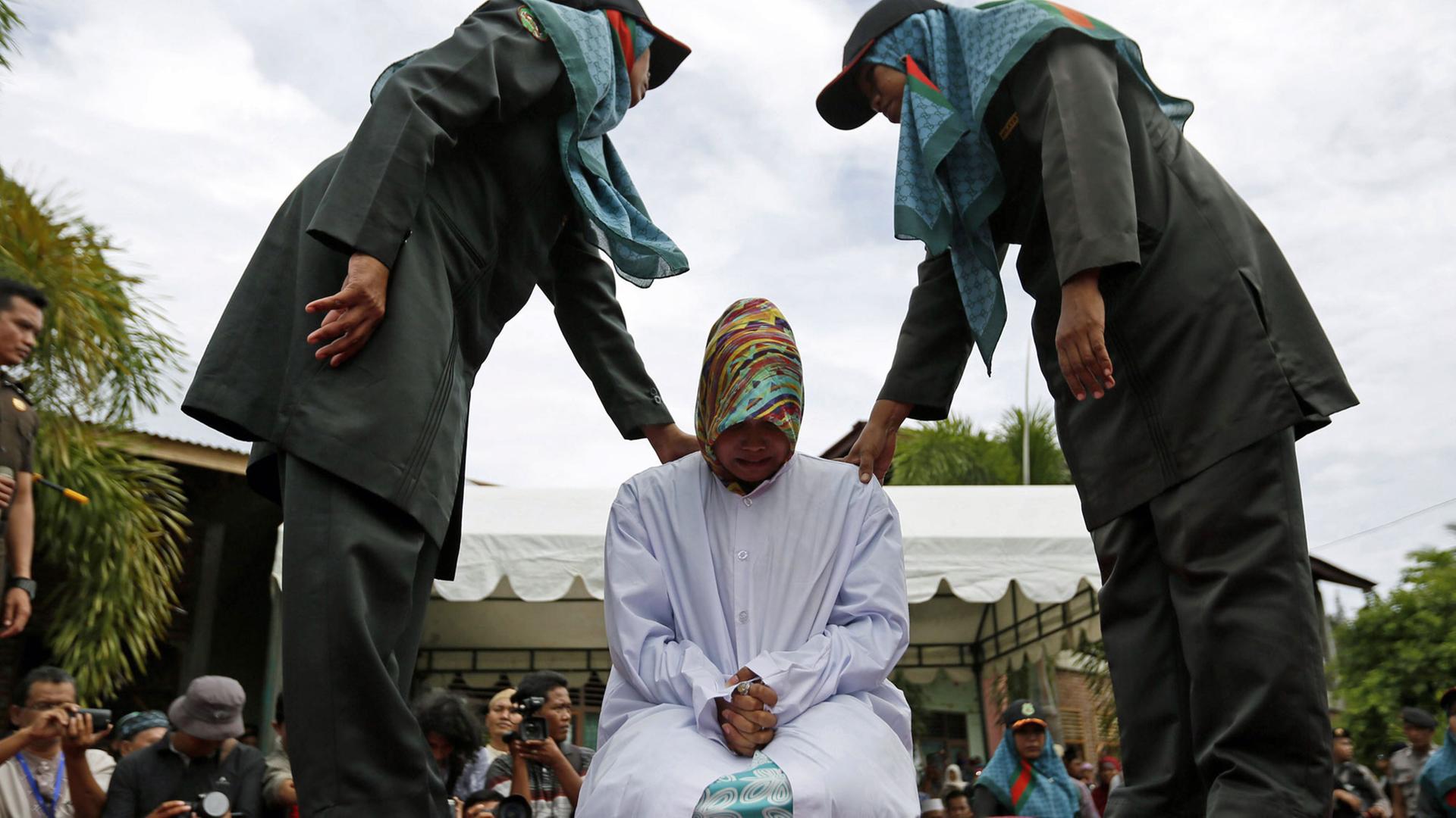 Sharia-Polizisten plazieren eine Frau zur öffentlichen Auspeitschung in Banda Aceh, Indonesien am 12. Juni 2015. Sharia-Polizisten plazieren eine Frau zur öffentlichen Auspeitschung in Banda Aceh, Indonesien am 12. Juni 2015.