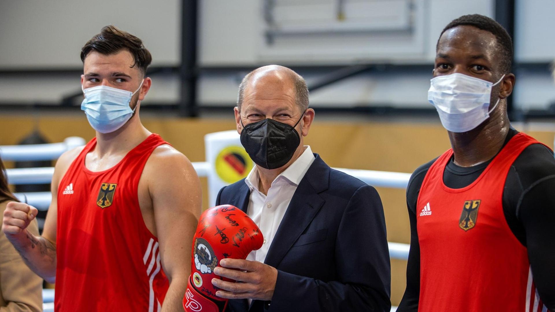 Olaf Scholz, Kanzlerkandidat der SPD für die Bundestagswahl, steht mit einem Boxhandschuh beim Besuch des Boxclub Traktor Schwerin im Boxring zwischen den Boxern Kevin Boakye-Schumann (r) und Deniel Krotter (l).