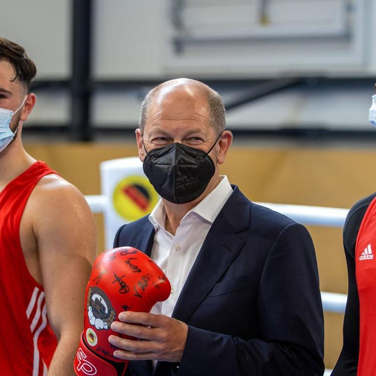 Olaf Scholz, Kanzlerkandidat der SPD für die Bundestagswahl, steht mit einem Boxhandschuh beim Besuch des Boxclub Traktor Schwerin im Boxring zwischen den Boxern Kevin Boakye-Schumann (r) und Deniel Krotter (l).