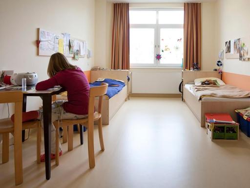 Eine Patientin der Kinder- und Jugendpsychiatrie Stadtroda sitzt in ihrem Zimmer und hat dem Betrachter den Rücken zugewandt.