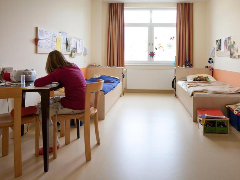 Eine Patientin der Kinder- und Jugendpsychiatrie Stadtroda sitzt in ihrem Zimmer und hat dem Betrachter den Rücken zugewandt.