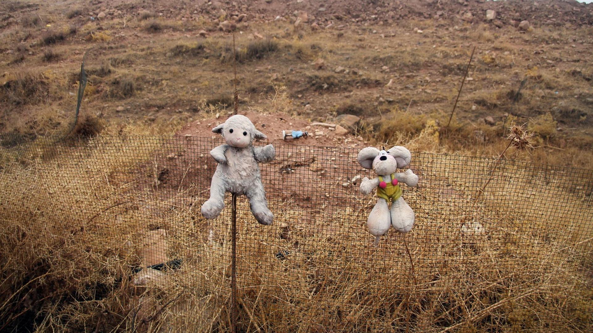 Zwei Kuscheltiere hängen an einem Zaun vor einem Massengrab nahe des Sindschar-Gebirges im Irak. Dort wurden Massengräber worden. Hier tötete die Terrormiliz IS massenhaft Jesiden. Zwei Kuscheltiere hängen an einem Zaun vor einem Massengrab nahe des Sindschar-Gebirges im Irak. Dort wurden Massengräber worden. Hier tötete die Terrormiliz IS massenhaft Jesiden.