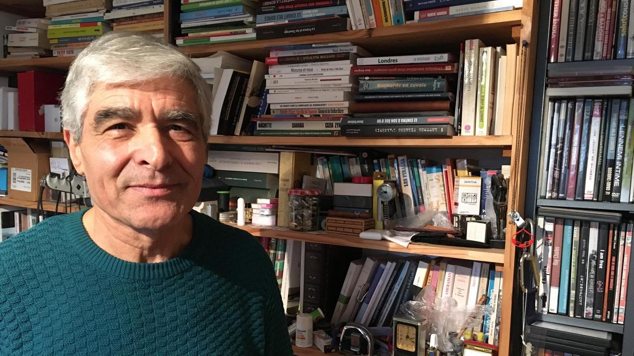 Der franko-algerische Journalis Larbi Benchiha steht vor einem Bücherregal.