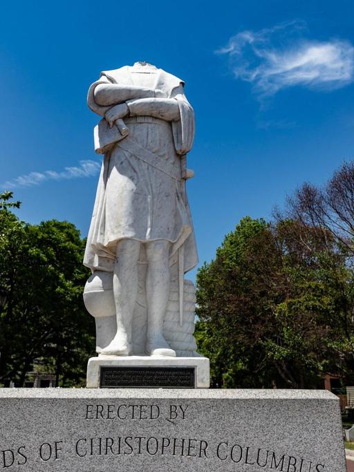 Kopflose weiße Statue vor blauem Himmel in einem Park.