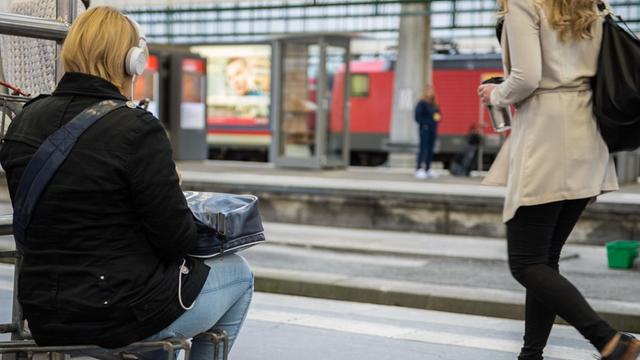 Eine Reisende sitzt im Hauptbahnhof Stuttgart auf einem Kofferkuli.