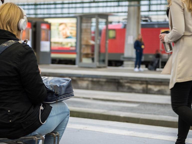 Eine Reisende sitzt im Hauptbahnhof Stuttgart auf einem Kofferkuli.