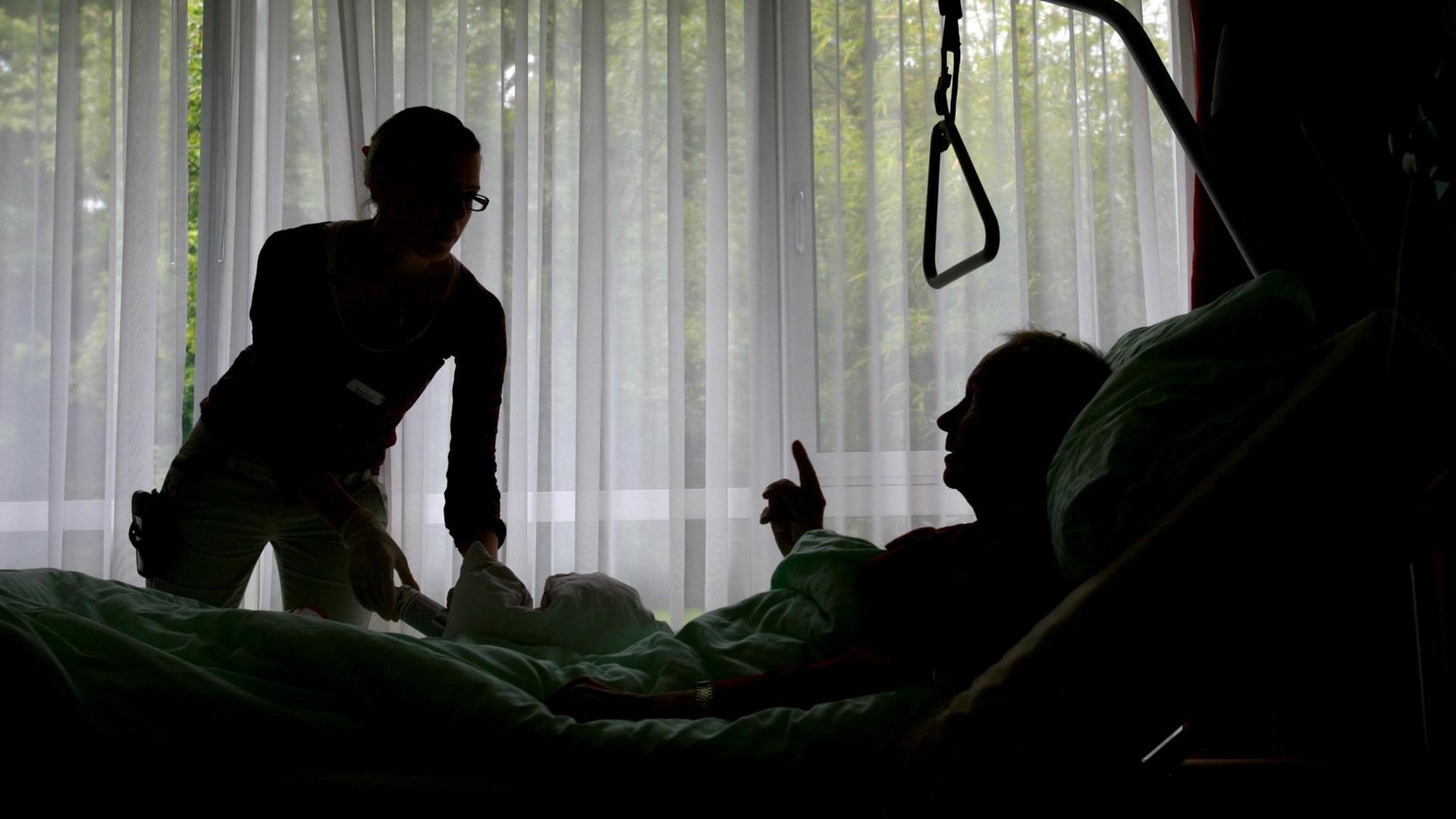 Eine Krankenpflegerin versorgt einen sterbenskranken Hospiz Bewohner, der im Bett liegt. Eine Krankenpflegerin versorgt einen sterbenskranken Hospiz Bewohner, der im Bett liegt.