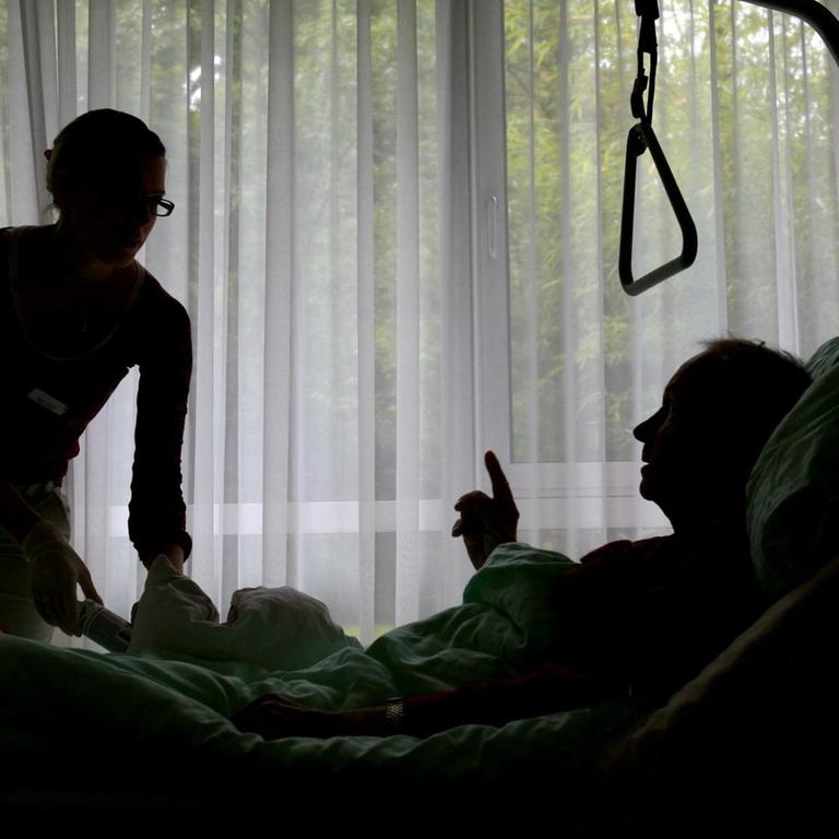 Eine Krankenpflegerin versorgt einen sterbenskranken Hospiz Bewohner, der im Bett liegt.