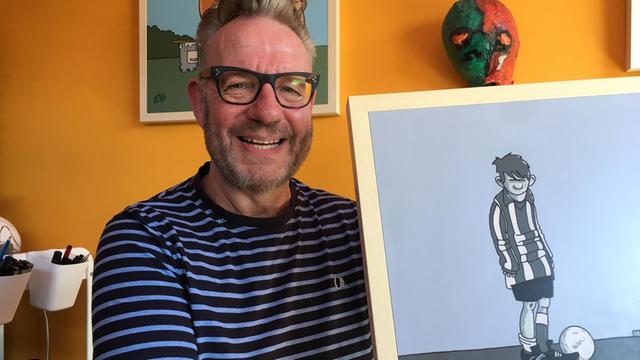 Der britische Zeichner Pete McKee hält in seinem Atelier in Sheffield ein Bild hoch mit einem grummeligen Fußballspieler