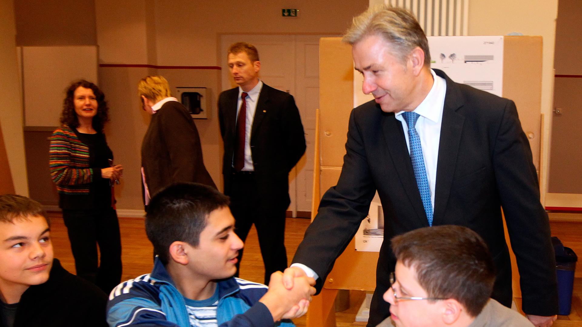 Klaus Wowereit steht in einem Klassenzimmer und schüttelt die Hand eines dunkelhaarigen Schülers. Klaus Wowereit steht in einem Klassenzimmer und schüttelt die Hand eines dunkelhaarigen Schülers.