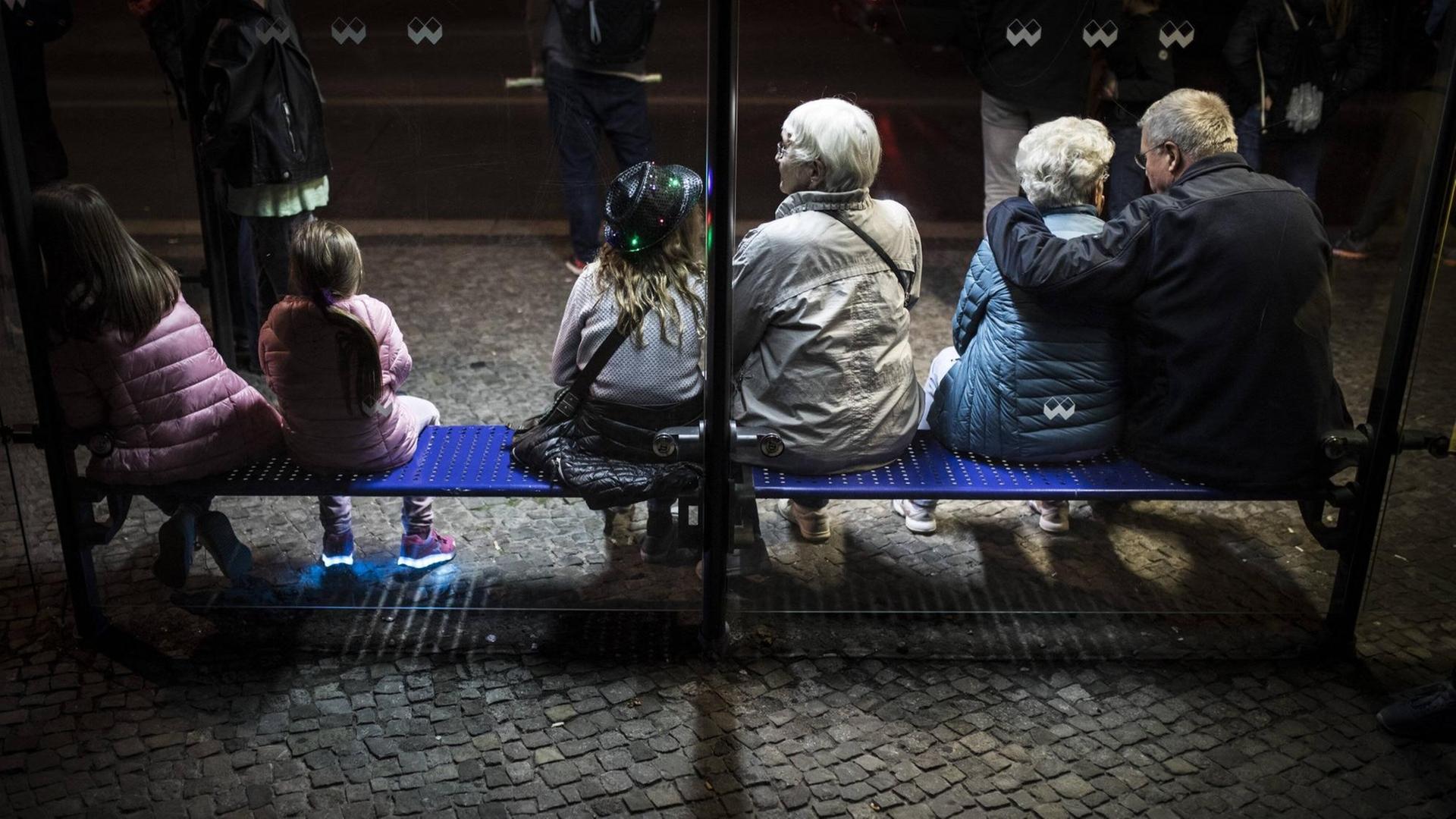 Drei Kinder und drei aeltere Menschen sitzen an einer Bushaltestelle in Berlin Drei Kinder und drei aeltere Menschen sitzen an einer Bushaltestelle in Berlin