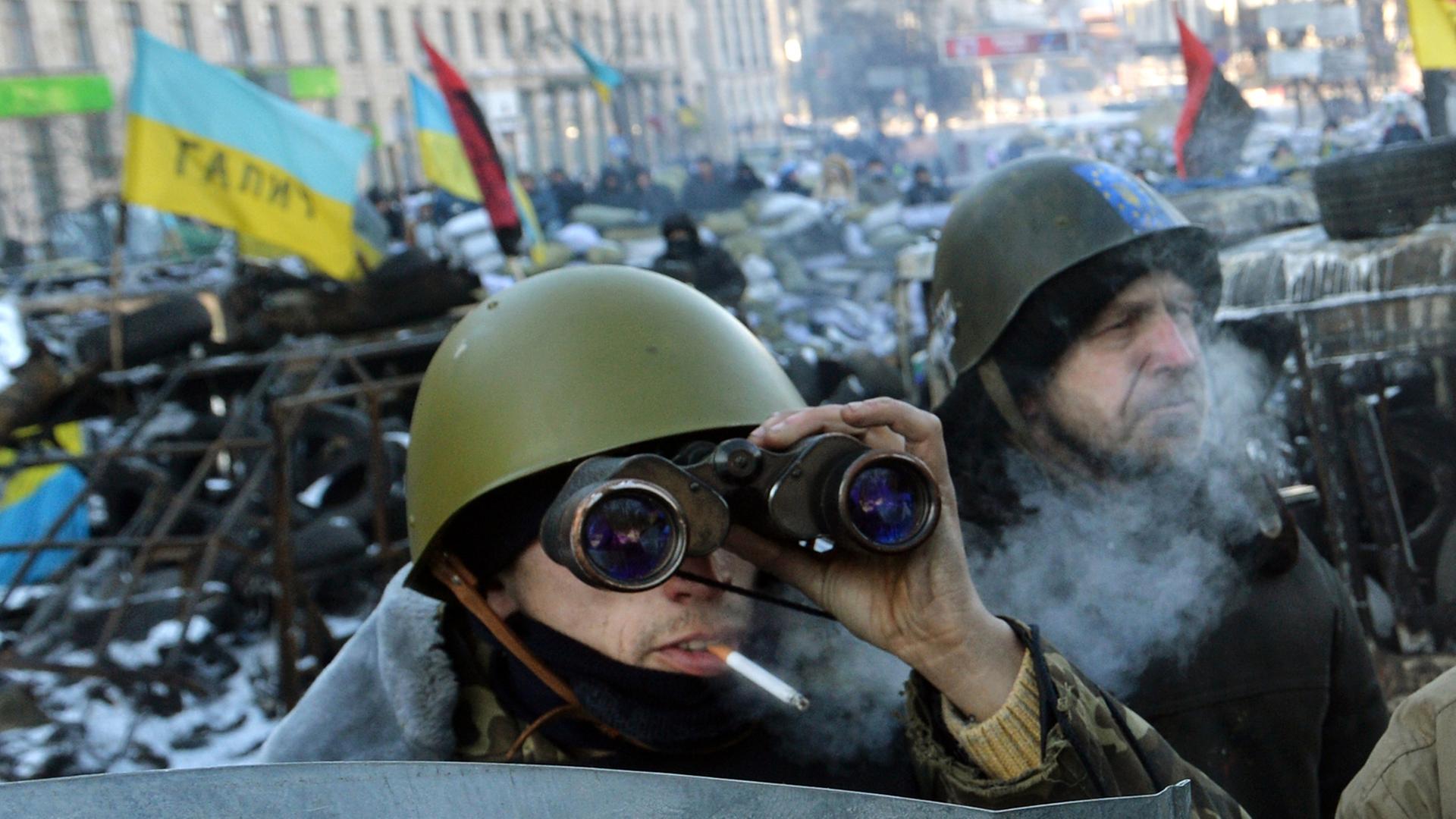 Ein Mann mit einem Fernglas beobachtet am 31. Januar 2014 von einer Barrikade der Opposition aus eine Straße in Kiew. Ein Mann mit einem Fernglas beobachtet am 31. Januar 2014 von einer Barrikade der Opposition aus eine Straße in Kiew.
