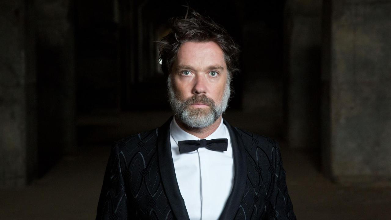 Der Musiker Rufus Wainwright steht in schwarzem Anzug mit Fliege vor einem schwarzen Hintergrund Der Musiker Rufus Wainwright steht in schwarzem Anzug mit Fliege vor einem schwarzen Hintergrund