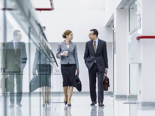 Eine Frau und ein Mann gehen einen Flur in einem Bürogebäude entlang