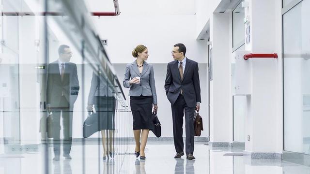 Eine Frau und ein Mann gehen einen Flur in einem Bürogebäude entlang