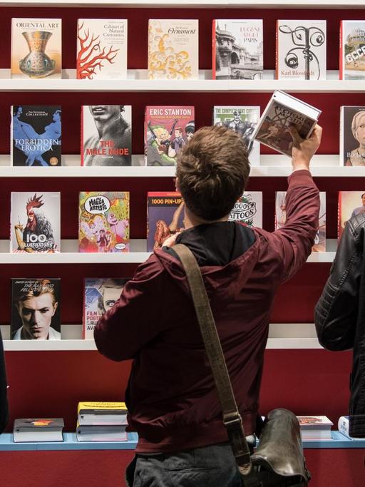 Besucher stehen auf der Buchmesse in Frankfurt am Main (Hessen) vor einem Bücherregal.