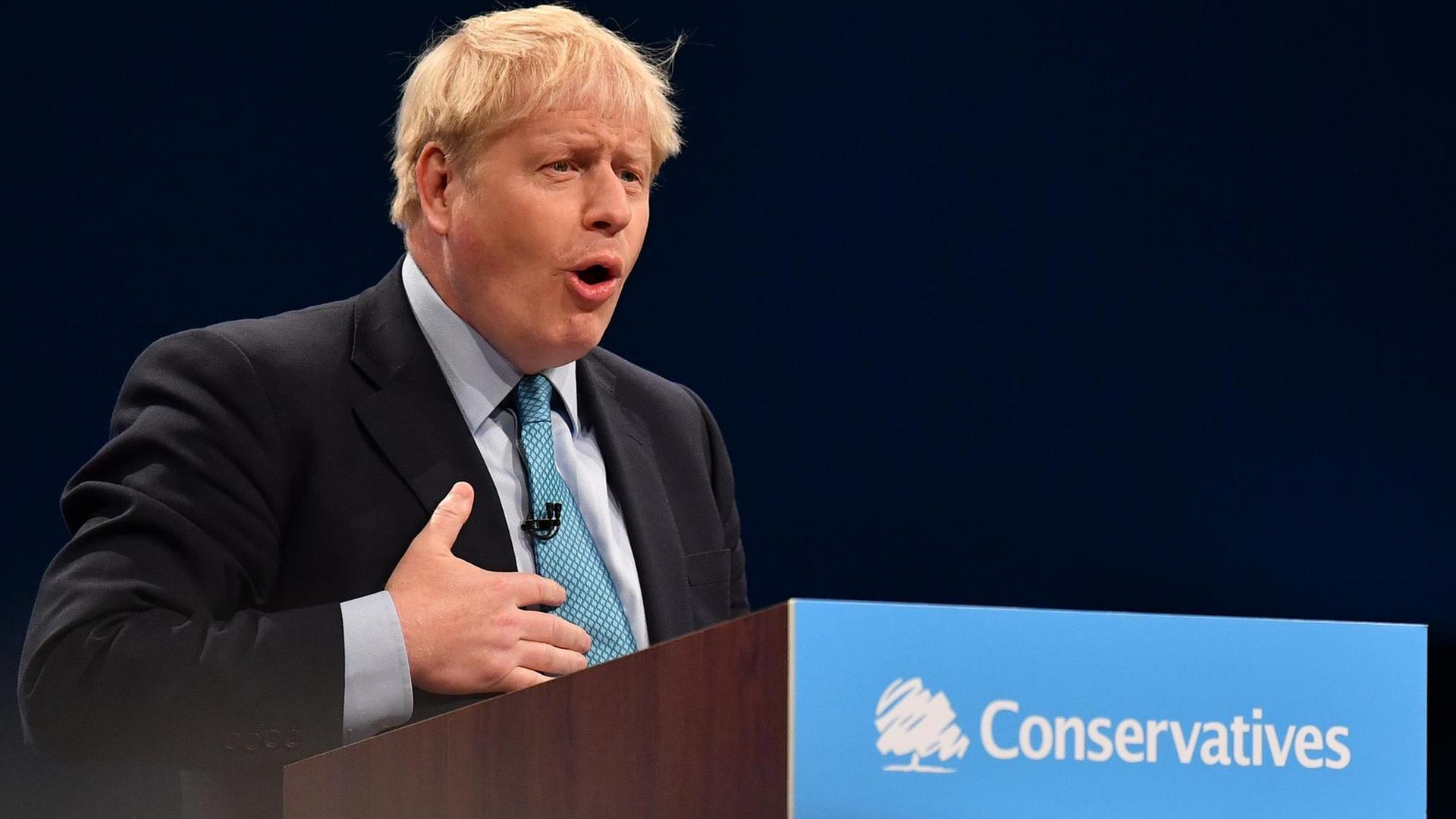 Der britische Premierminister Boris Johnson auf dem Parteitag in Manchester. Er steht hinter einem Rednerpult. Der britische Premierminister Boris Johnson auf dem Parteitag in Manchester. Er steht hinter einem Rednerpult.