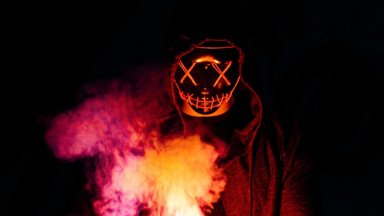 Symbolbild für Dämonen: eine Gestalt mit gruselige Maske unter einer Kapuze mit Feuer in der Hand. Symbolbild für Dämonen: eine Gestalt mit gruselige Maske unter einer Kapuze mit Feuer in der Hand.