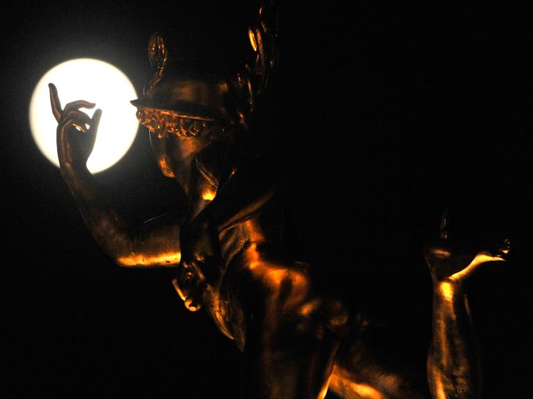 Die Statue des Merkur auf der Alten Kanzlei in Stuttgart scheint nach dem Mond zu greifen.
