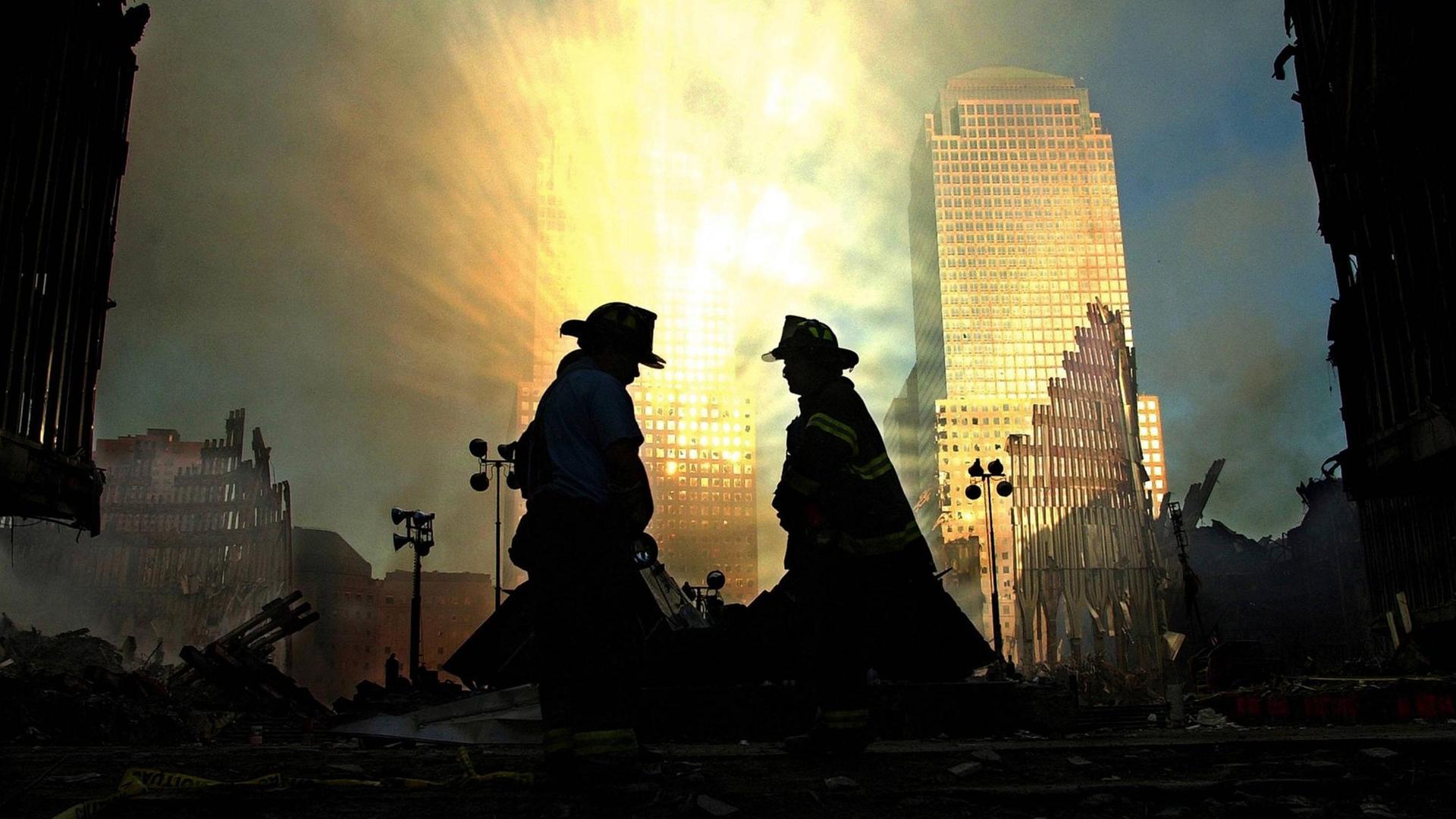 Vor reflektierenden Lichtstrahlen setzen sich die Silhouetten zweier Feuerwehrmänner ab, die die Zerstörung am Ground Zero begutachten.
