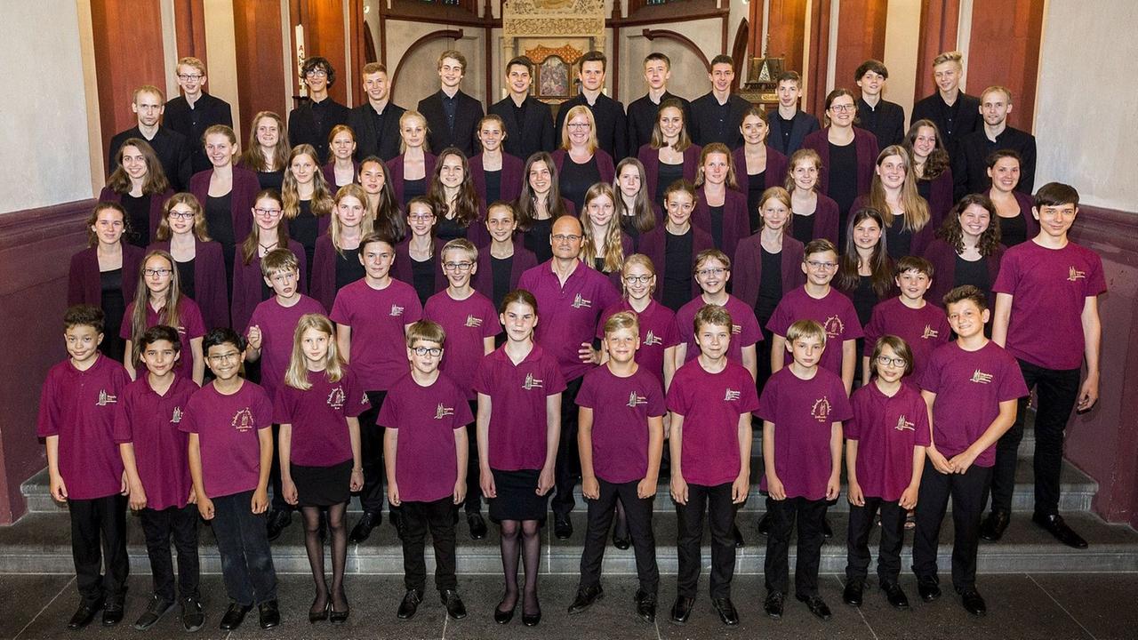 Die Sängerinnen und Sänger stehen in lila Chor-T-Shirts in einer Kirche. Die Sängerinnen und Sänger stehen in lila Chor-T-Shirts in einer Kirche.
