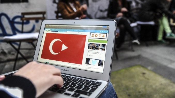 Jemand hat einen Computer auf dem Schoß. Auf dem Monitor sind eine Videoplattform und eine türkische Flagge zu sehen.