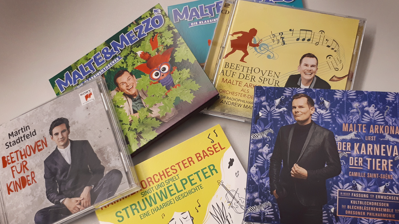 Auf einem Tisch liegen mehrere CD-Hartplastikhüllen übereinander. Die Cover zeigen bunte Motive mit Gesichtern von Männern und Cartoons. Auf einem Tisch liegen mehrere CD-Hartplastikhüllen übereinander. Die Cover zeigen bunte Motive mit Gesichtern von Männern und Cartoons.