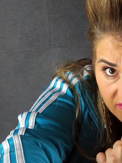 Die Schauspielerin und Kabarettistin Idil Baydar in ihrer Rolle als Jilet Ayse, autoupierter Pony, böser Blick in die Kamera, die Faust geballt (aufgenommen 2015 in Berlin)