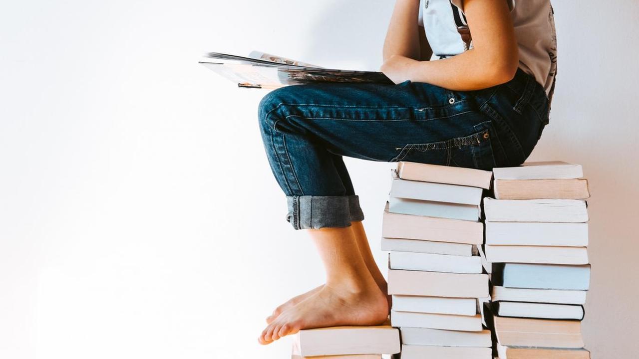Ein Kind sitzt auf einem großen Bücherstapel und liest. Ein Kind sitzt auf einem großen Bücherstapel und liest.