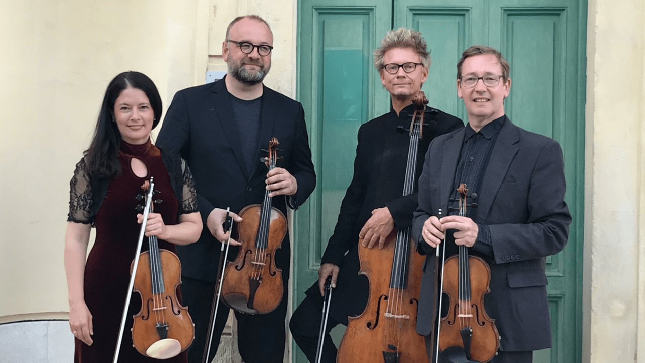 Eine Geigerin und drei weitere Musiker stehen mit ihren Instrumenten in Konzertkleidung von einer grünen, historischen Rassettentür. Eine Geigerin und drei weitere Musiker stehen mit ihren Instrumenten in Konzertkleidung von einer grünen, historischen Rassettentür.