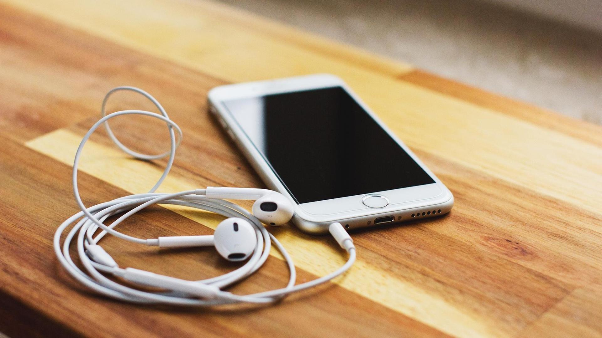 Auf einem Tisch liegt ein weißes Smartphone mit weißen Kopfhörern. Auf einem Tisch liegt ein weißes Smartphone mit weißen Kopfhörern.
