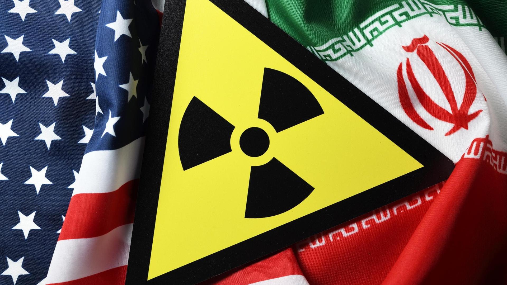 Eine Bildkollage auf der die Fahnen der USA und des Iran sowie ein Radioaktivitätwarnschild zu sehen sind. Eine Bildkollage auf der die Fahnen der USA und des Iran sowie ein Radioaktivitätwarnschild zu sehen sind.