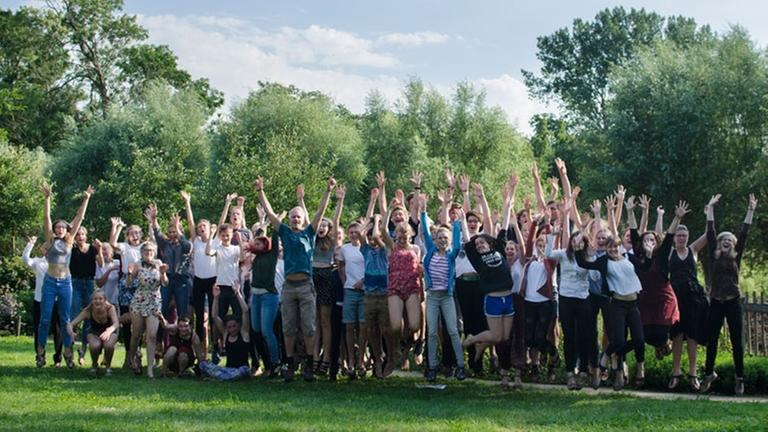 Ein Gruppenbild des Chores auf einer Wiese. Die Jugendlichen springen hoch und strecken die Arme empor. Ein Gruppenbild des Chores auf einer Wiese. Die Jugendlichen springen hoch und strecken die Arme empor.