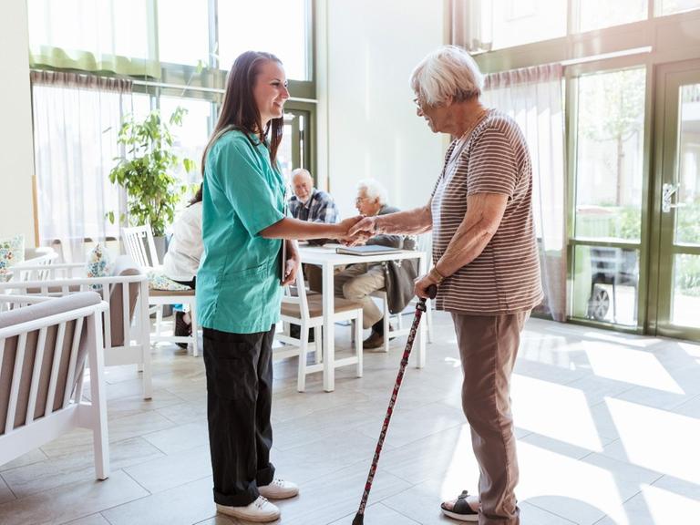 Eine Pflegerin begrüßt eine ältere Frau in einem Seniorenheim.