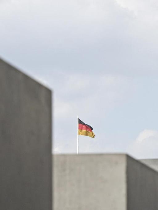 Zwischen den Stelen des Mahnmals für die ermordeten Juden in Berlin ist eine Deutschland-Fahne zu sehen.