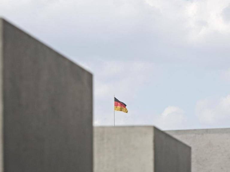 Zwischen den Stelen des Mahnmals für die ermordeten Juden in Berlin ist eine Deutschland-Fahne zu sehen.