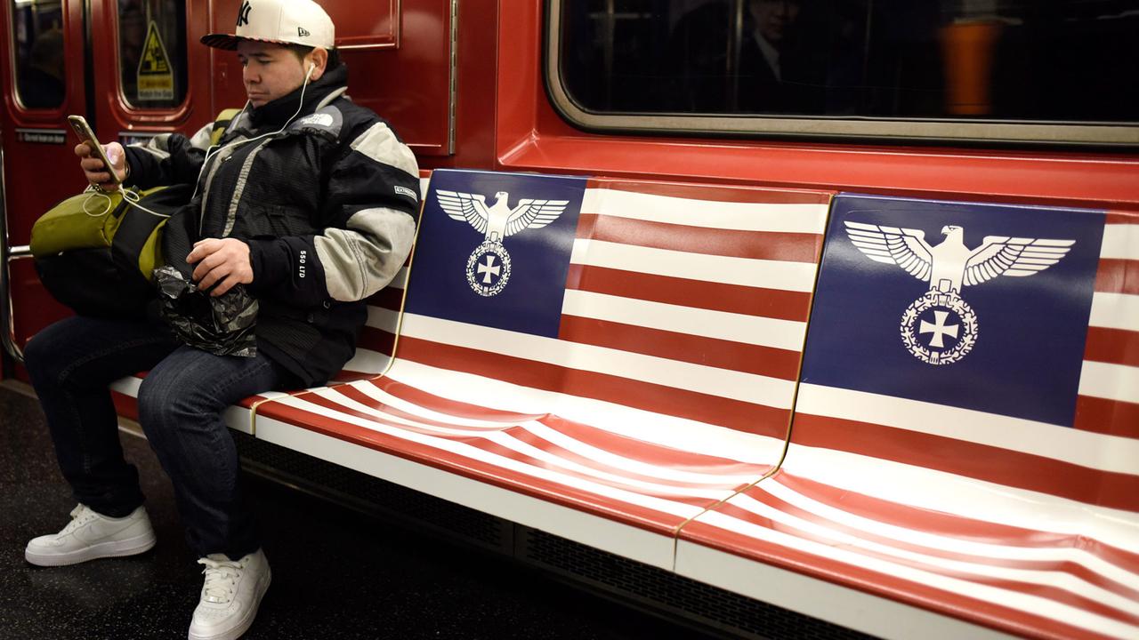 Ein Mann sitzt in der New-Yorker-U-Bahn, die Sitze sind mit einem abgewandelten "Reichsadler" beklebt. Damit wurde die Amazon-Serie "Man in the High Castle" beworben. Ein Mann sitzt in der New-Yorker-U-Bahn, die Sitze sind mit einem abgewandelten "Reichsadler" beklebt. Damit wurde die Amazon-Serie "Man in the High Castle" beworben.