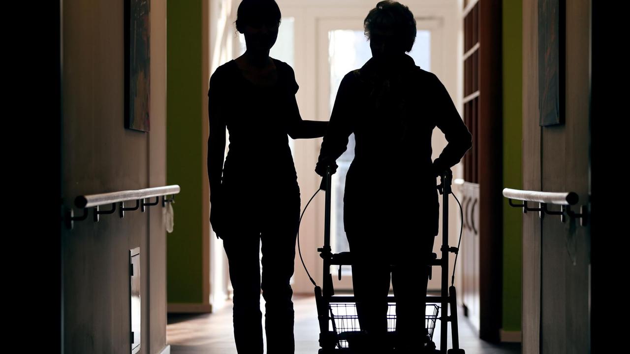 ARCHIV - Eine Pflegekraft (l) begleitet am 22.02.2013 die Bewohnerin eines Altenheims mit Rollator beim Gang über den Flur. Seit Jahren bauen Krankenhäuser Pflegestellen ab, trotz steigender Patientenzahlen. Nun zeigt ein Bericht des Statistischen Bundesamtes, wie dramatisch die Situation des Pfleger in Thüringen ist. (zu dpa «Arbeitsbelastung für Pflegekräfte in Thüringen gestiegen» vom 05.10.2017) Foto: Oliver Berg/dpa +++(c) dpa - Bildfunk+++ | Verwendung weltweit ARCHIV - Eine Pflegekraft (l) begleitet am 22.02.2013 die Bewohnerin eines Altenheims mit Rollator beim Gang über den Flur. Seit Jahren bauen Krankenhäuser Pflegestellen ab, trotz steigender Patientenzahlen. Nun zeigt ein Bericht des Statistischen Bundesamtes, wie dramatisch die Situation des Pfleger in Thüringen ist. (zu dpa «Arbeitsbelastung für Pflegekräfte in Thüringen gestiegen» vom 05.10.2017) Foto: Oliver Berg/dpa +++(c) dpa - Bildfunk+++ | Verwendung weltweit