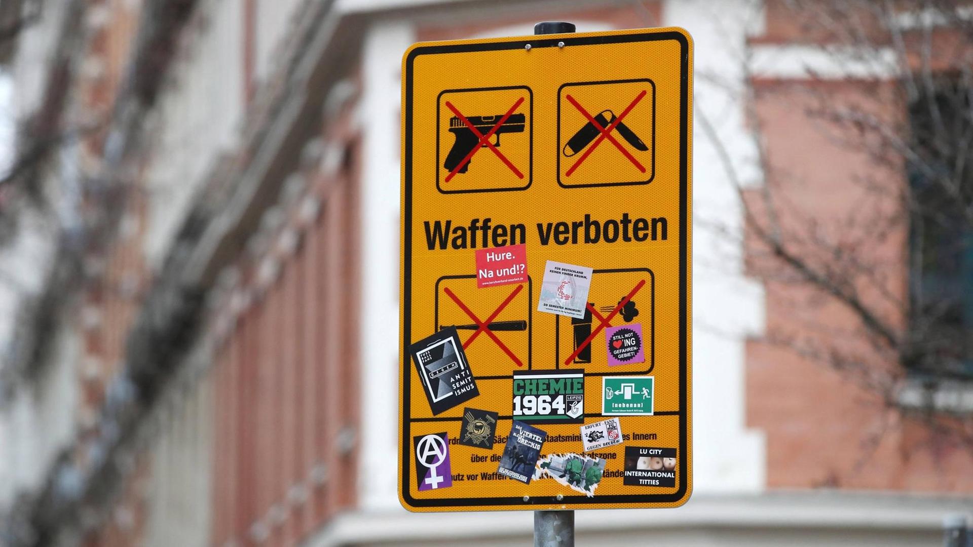 Ein gelbes Schild mit der Aufschrift "Waffen verboten" und der Darstellung von, mit roten Kreuzen markierten, Piktogrammen einer Schusswaffe, eines Klappmessers, eines Schlägers und eines Pfeffersprays. Ein gelbes Schild mit der Aufschrift "Waffen verboten" und der Darstellung von, mit roten Kreuzen markierten, Piktogrammen einer Schusswaffe, eines Klappmessers, eines Schlägers und eines Pfeffersprays.