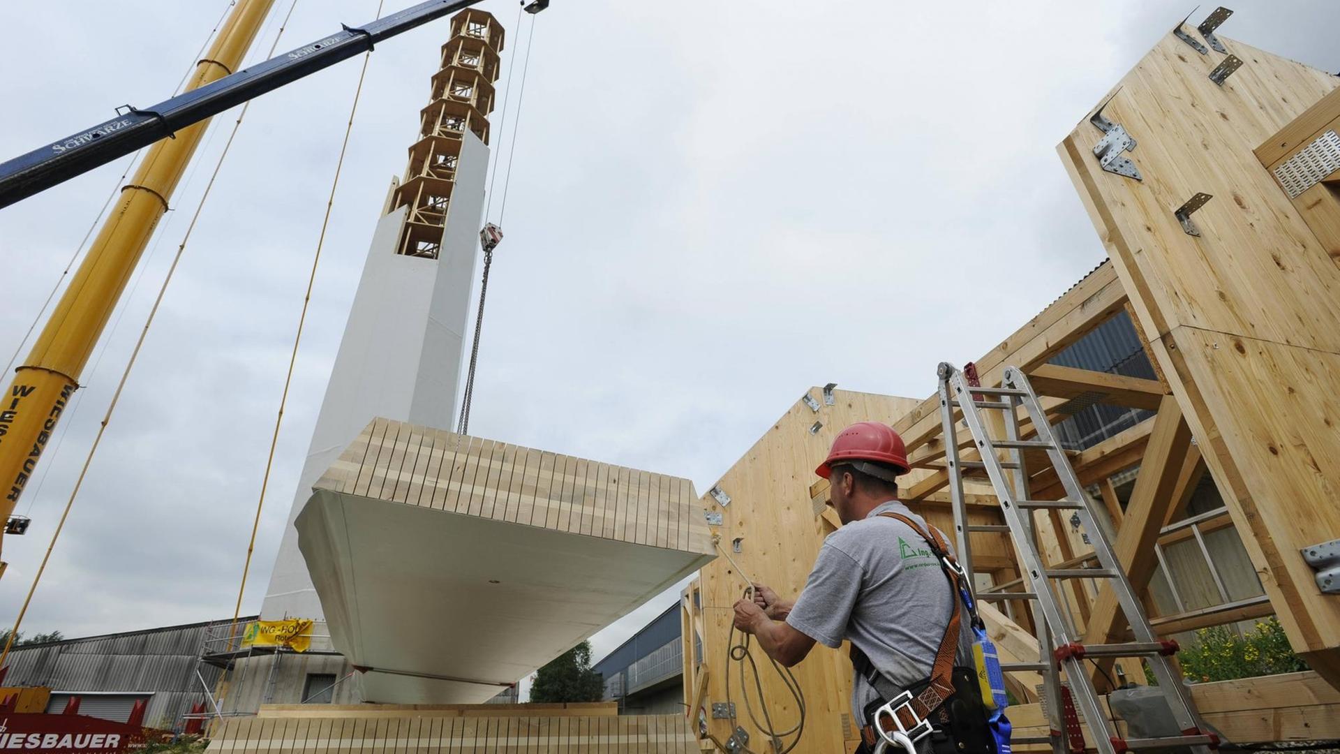 Ein Bauarbeiter richtet ein Paneel für die Windkraftanlage aus Holz auf. Ein Bauarbeiter richtet ein Paneel für die Windkraftanlage aus Holz auf.