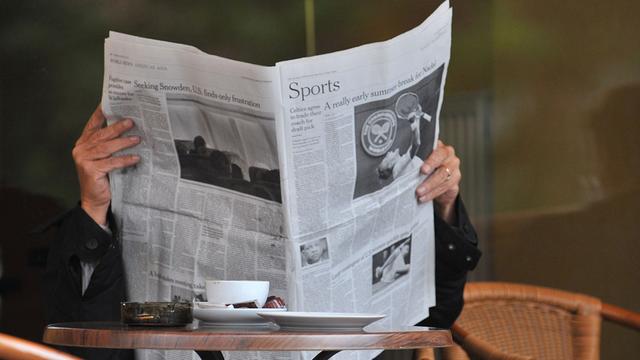Ein Mann sitzt in einem Cafe und liest eine Zeitung.