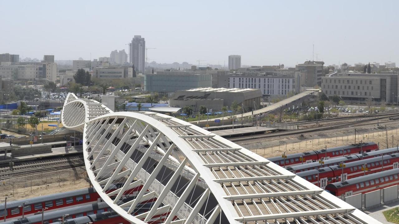 Eine weiße Brücke verläuft über Bahngleise vom Technologiepark auf den Campus der Ben Gurion Universität.