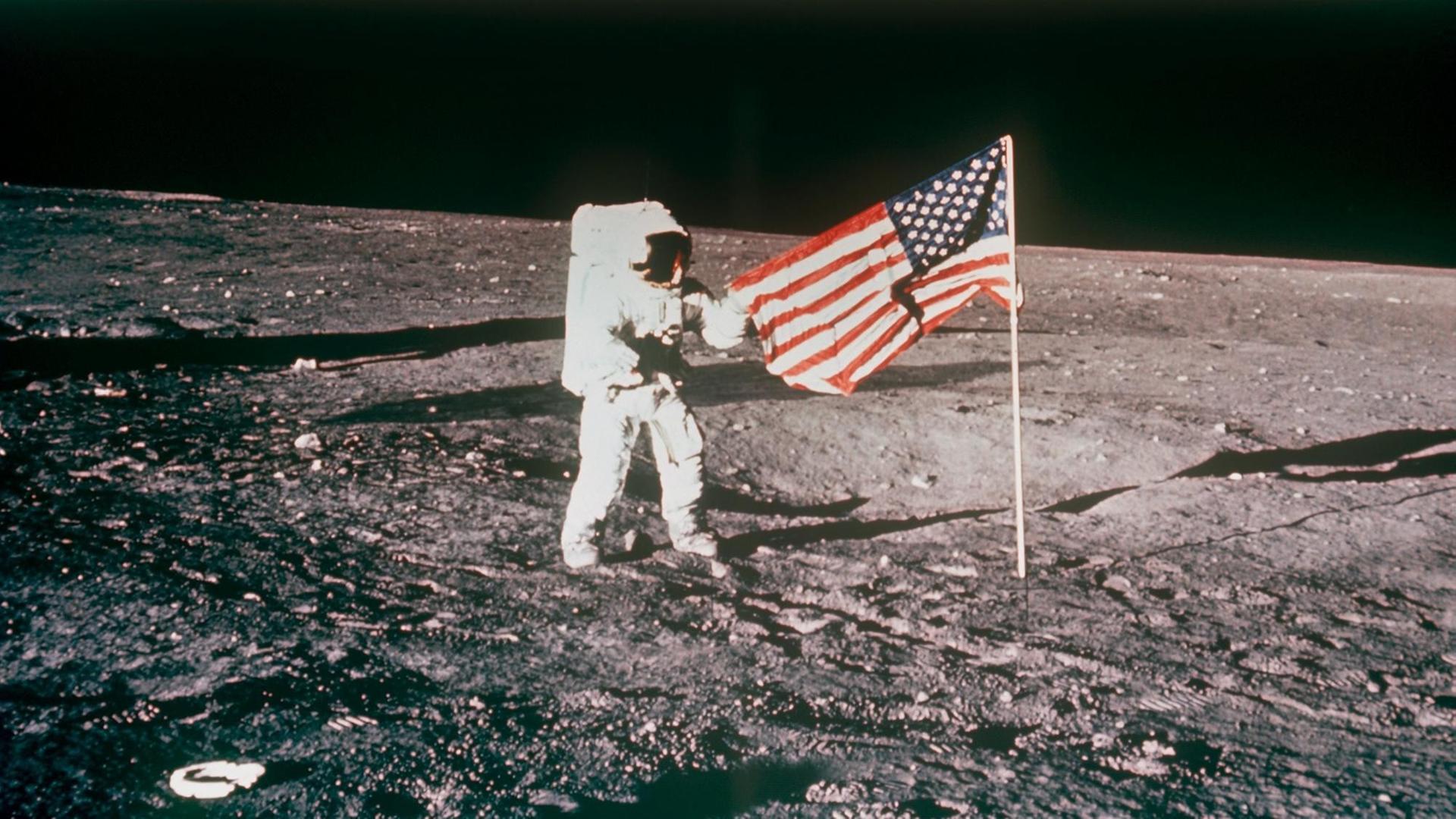 Ein Astronaut der Apollo-12-Besatzung hisst die US-amerikanische Flagge auf dem Mond. Ein Astronaut der Apollo-12-Besatzung hisst die US-amerikanische Flagge auf dem Mond.