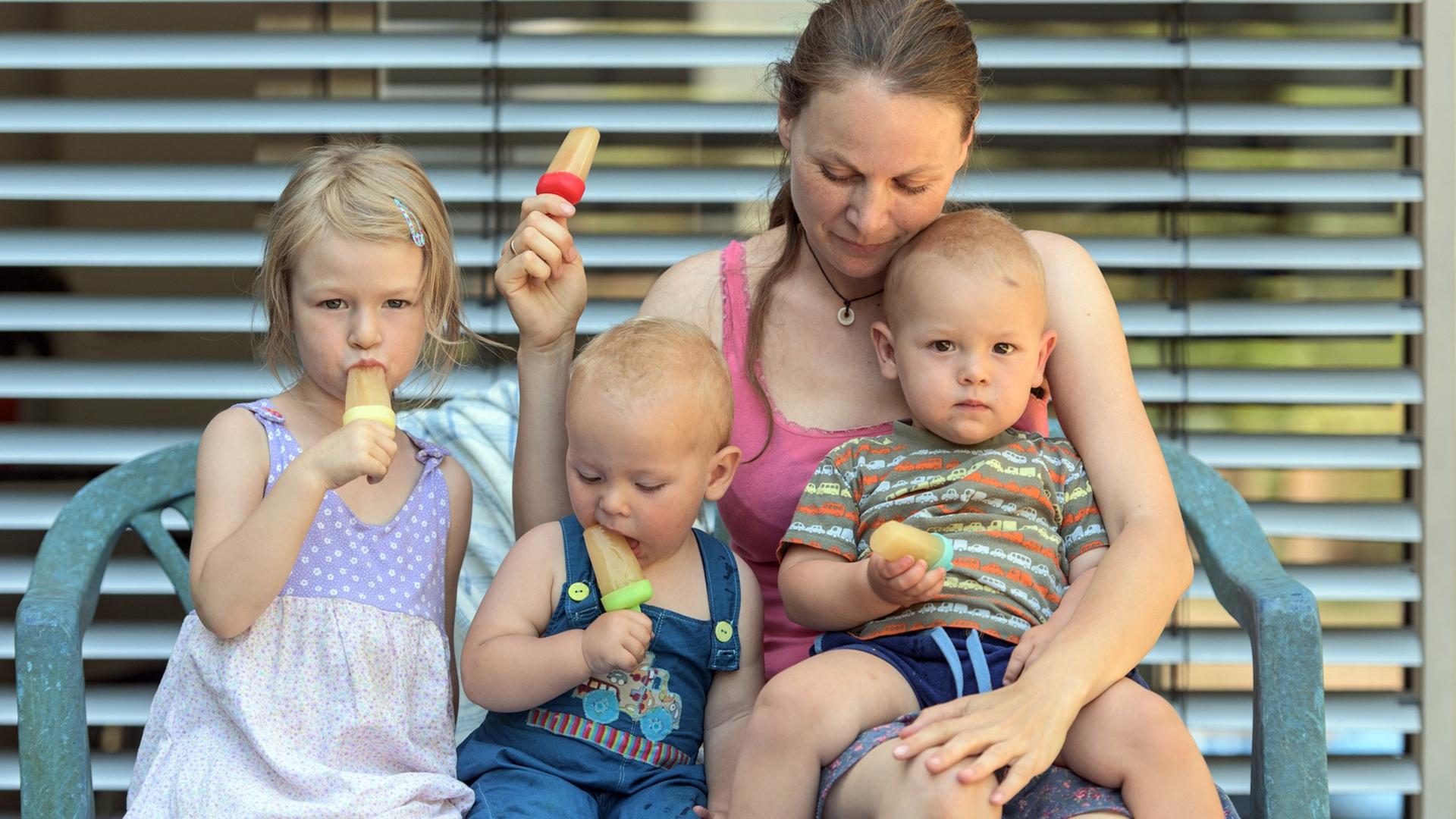 Eine Mutter mit drei Kindern sitzt in Freiburg im Breisgau im Garten und isst Eis Eine Mutter mit drei Kindern sitzt in Freiburg im Breisgau im Garten und isst Eis