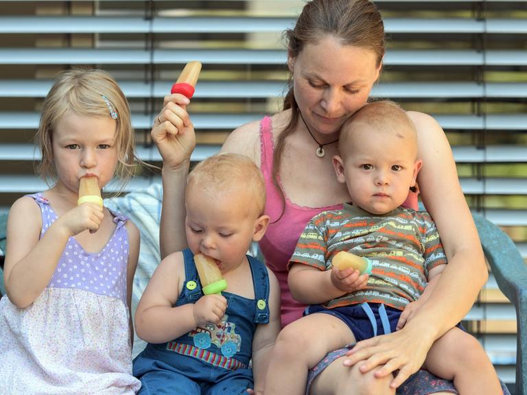 Eine Mutter mit drei Kindern sitzt in Freiburg im Breisgau im Garten und isst Eis