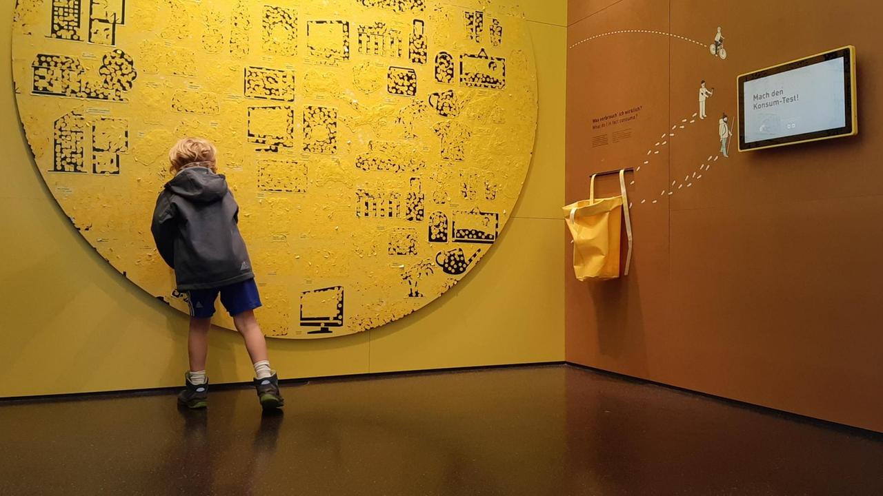 Ein Junge steht vor einer gelben Wand und klebt Punkte auf die Bilder eines Autos oder ein Flugzeugs.