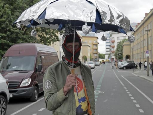 Ein Demonstrant mit Maske und Aluminiumschirm steht auf der Straße in Berlin.