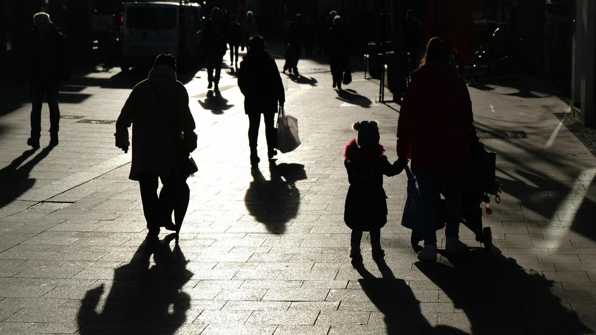Passanten mit Tüten gehen während des Lockdowns durch eine Fußgängerzone und sind dabei als Silhouette und Schatten zu sehen. Passanten mit Tüten gehen während des Lockdowns durch eine Fußgängerzone und sind dabei als Silhouette und Schatten zu sehen.